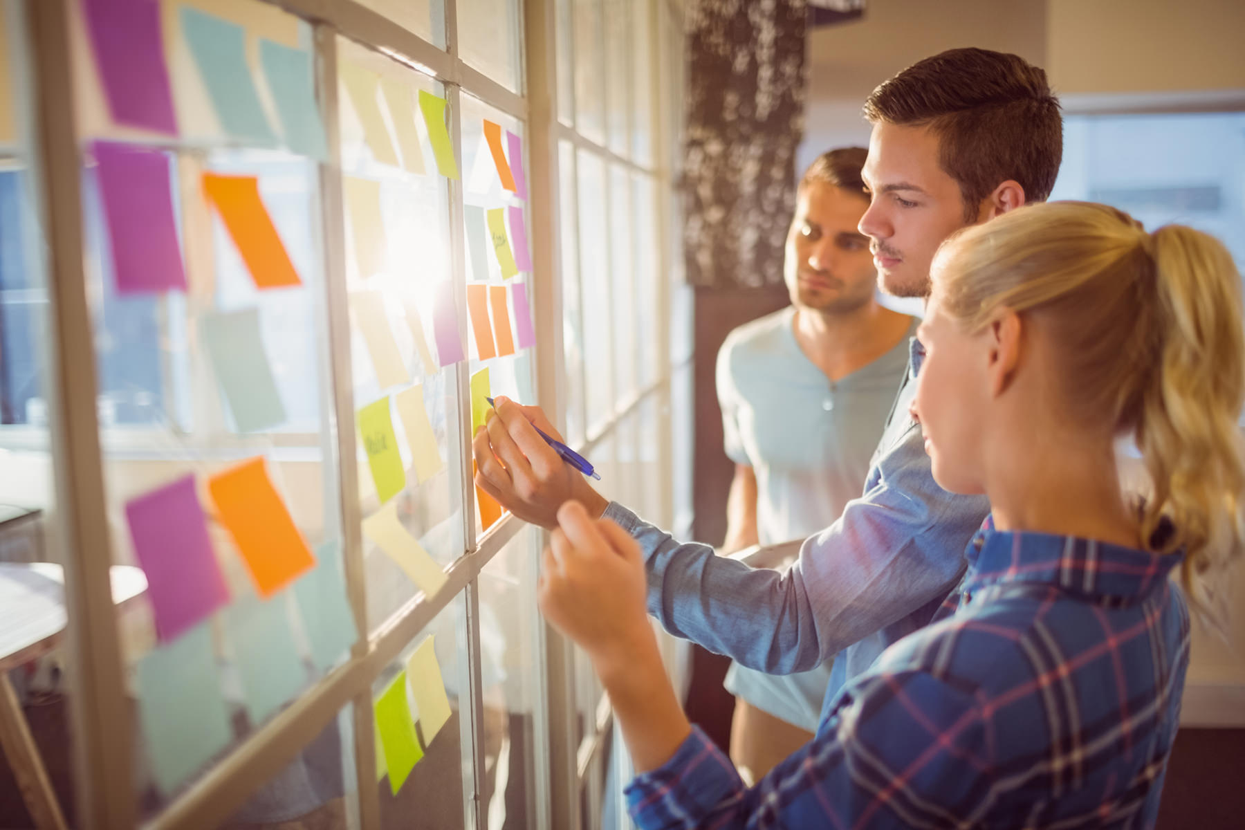 three people adding sticky notes to a window